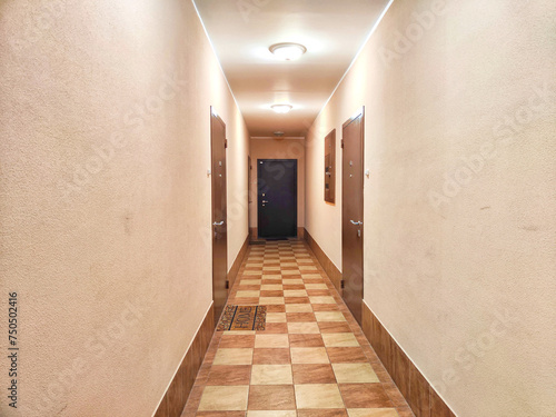 A corridor with wooden doors and a checkered floor pattern. Warmly Lit Hotel Corridor With Checkered Floor Design