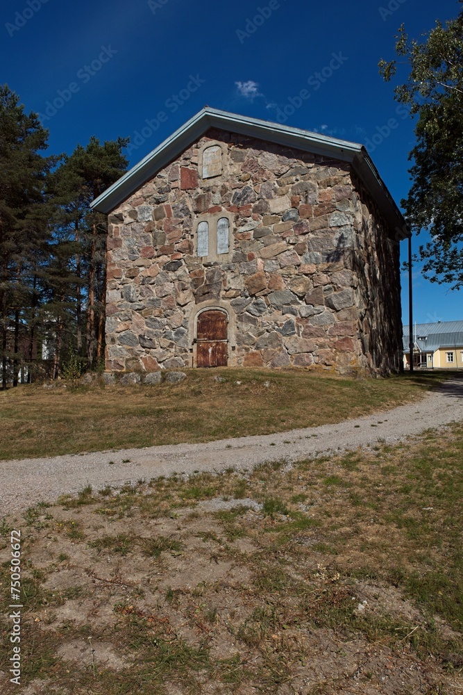 Fototapeta premium Old stone building with barred metal door and covered windows in summer.