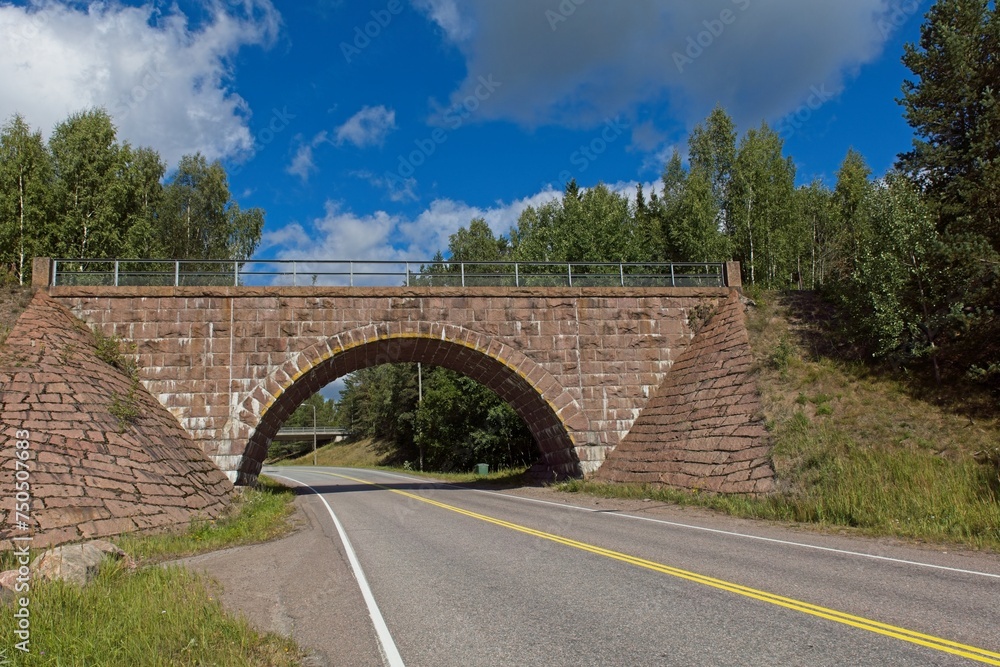 Old arch bridge made of stone over Turuntie road in summer with clouds in the sky, Myllylampi, Nummela, Finland.