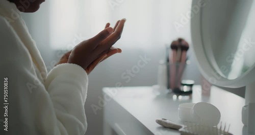 African woman sitting in front of mirror, applying cream on her hands.