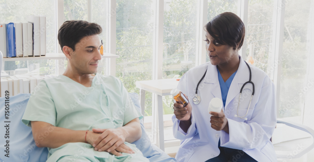 Portrait patient caucasian man lying bed with woman doctor sitting carer physical therapist African-American two people talk helping support explain medicine sick person inside hospital room service. Portrait patient caucasian man lying bed with woman doctor sitting carer physical therapist African-American two people talk helping support explain medicine sick person inside hospital room service.