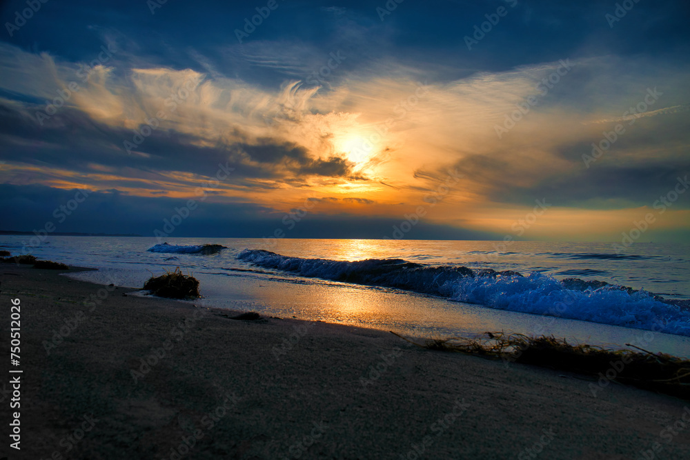 Sunset, illuminated sea. Sandy beach in the foreground. Light waves. Baltic Sea