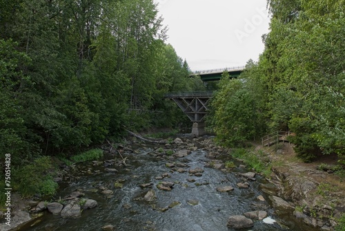 Landscape view of river Vantaanjoki with bridge crossing, rocks, trees and foliage in summer, Myllykoski, Nurmijärvi, Finland. photo