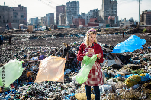 Woman on landfill hanging plastic bags as laundry. Consumerism versus plastic pollution concept. photo