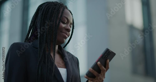 Black woman standing outside, using smartphone, reading online messages.