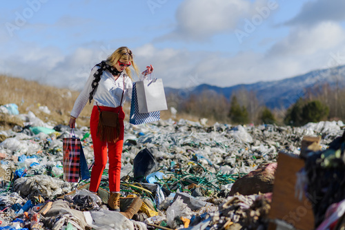 Modern woman on landfill with shopping bags. consumerism versus pollution concept. photo