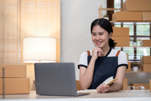 young female entrepreneur writes on the front of a product box to sell products online and prepares to send them to customers. Online selling at home, working from home © wichayada