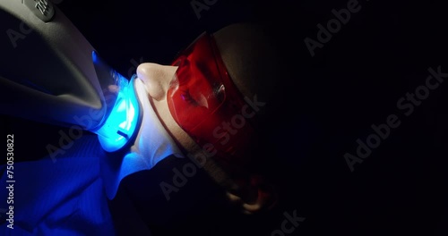 Teeth whitening procedure with ultraviolet light UV lamp in a modern clinic. Female patient in protective glasses at dentist chair. Whitening light bleaching woman teeth. Cosmetic dentistry center. photo
