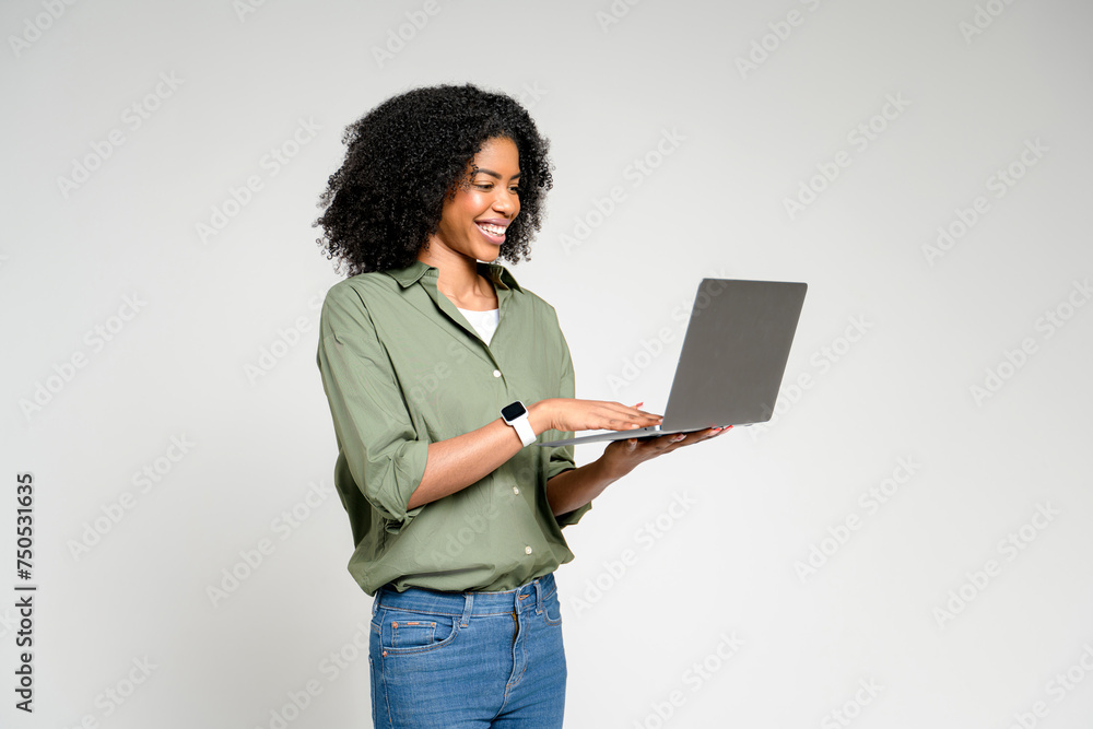 African-American woman with a warm smile working on her laptop standing isolated, representing the fusion of work and comfort in a modern home setting, complete with minimalist aesthetics. African-American woman with a warm smile working on her laptop standing isolated, representing the fusion of work and comfort in a modern home setting, complete with minimalist aesthetics.