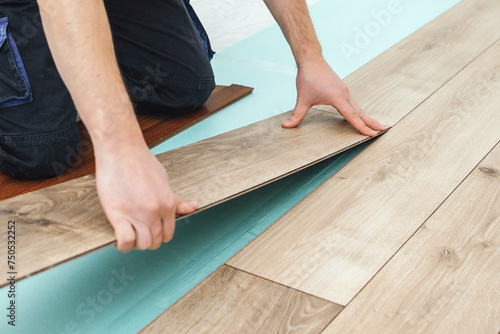 Worker installing new laminated wooden floor. Easy and quick installation of the flooring. Connecting laminate locks. DIY floating floor.