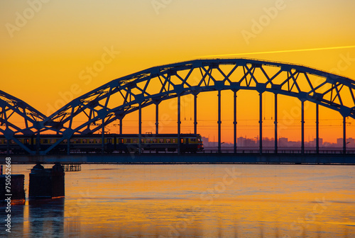Fototapeta Naklejka Na Ścianę i Meble -  A beautiful sunrise scenery with iron bridge over the frozen river Daugava in Latvian capital city Riga. Winter landscape of Northern Europe.