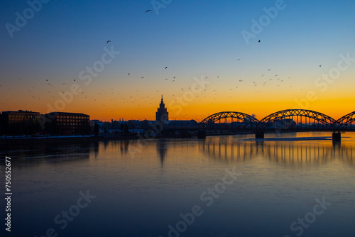A beautiful sunrise scenery with iron bridge over the frozen river Daugava in Latvian capital city Riga. Winter landscape of Northern Europe. © dachux21