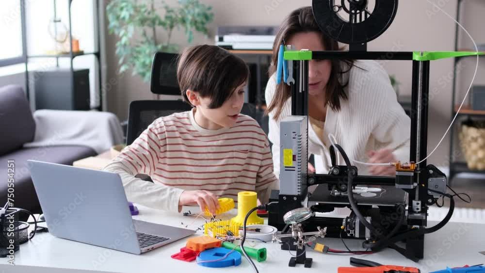 Curious Caucasian son and mother control work of a 3D printer together ...