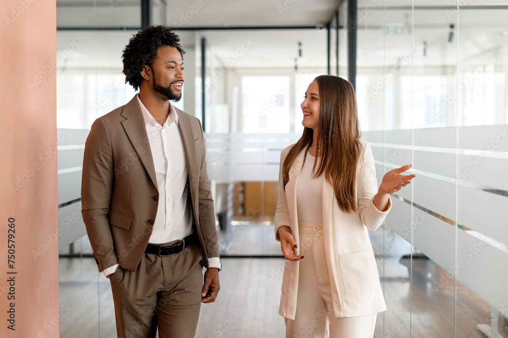 In a modern office corridor, an African-American businessman and his colleague are engaged in a lively discussion, walking together In a modern office corridor, an African-American businessman and his colleague are engaged in a lively discussion, walking together