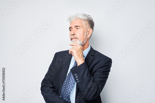Thoughtful senior businessman hand on chin, contemplating isolated on a light background. © amixstudio