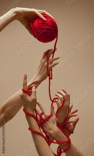 Friendship. Hand holds ball of threads and hands nearby unravel this tangle, intertwining and uniting against sandy color studio background. Concept of human touch, beauty and care, spa procedures.