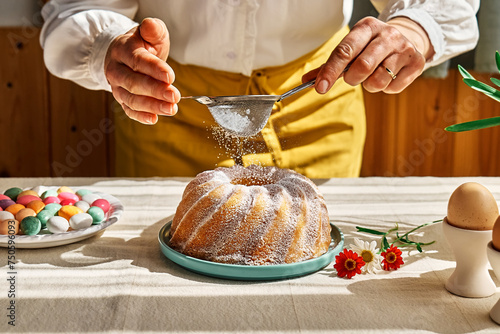 Foto Female hands sprinkles Easter cake with icing sugar through sieve