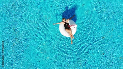  Woman relaxing in pool float unicorn inflatable ring floating on turquoise pool water. Aerial top view from drone.