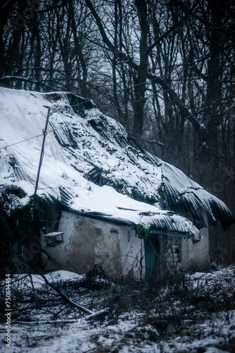 Abandoned house in the forest village at winter. Mystery landscape archittcture. Evening at village. Snow on the roof photo