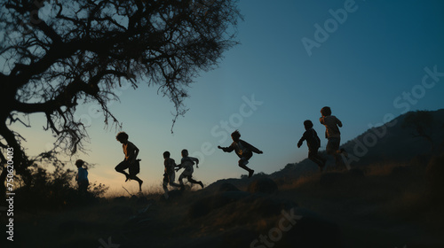 Silhouettes of people with sunset light in nature they run along the top against the background of the sky and a tree in the evening, children rejoice