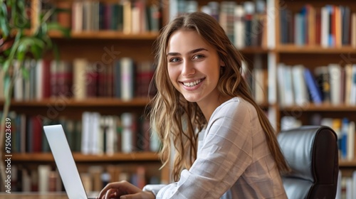 Smiling young woman lawyer, notary works in the office at the laptop, with bookshelf background photo