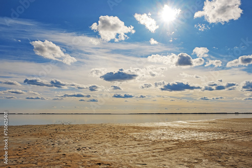 Beautiful shore of lake, clouds on sky and reflections on water surface. Summer sunlight day. Vibrant colored landscape, salt lake with footprints foots on marshy shore, sunlight glare