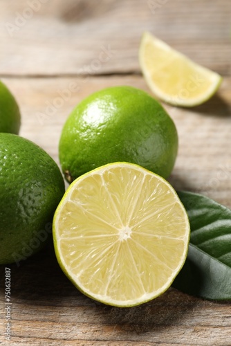 Whole and cut fresh limes on wooden table, closeup