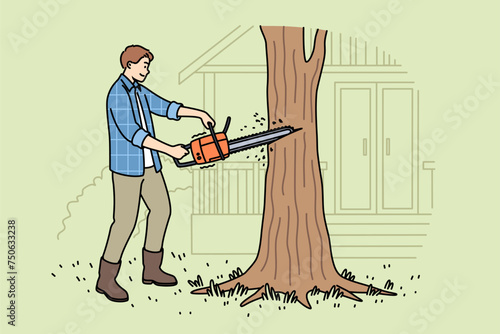 Man lumberjack uses chainsaw to get rid of old, diseased tree growing near house. Young guy works as lumberjack and helps residents of country cottages clear area of unnecessary trees.