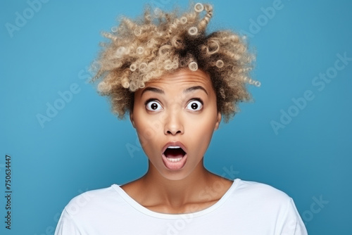 A beautiful African American woman with a short haircut is surprised on a blue background. 