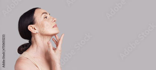 Beautiful senior woman with lifting arrows showing facial anti-aging treatment on skin against grey studio background. Negative space. Concept of beauty procedures, cosmetology treatment, massage. Ad