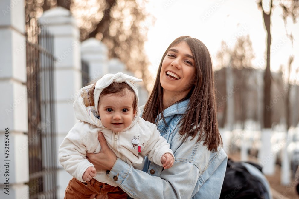Obraz premium A young happy dark-haired woman carries her one-year-old daughter in her arms while walking.A family concept.Happy motherhood.