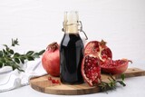 Tasty pomegranate sauce in bottle, branches and fruits on light table, closeup