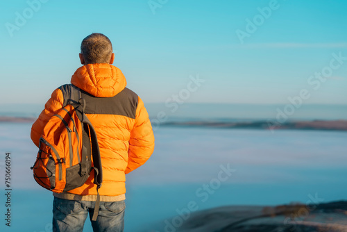 elderly mature man enjoying life at full by travelling around world sitting on the top of mountains against sky and clouds on cold sunny winter soring day. Travel Lifestyle concept