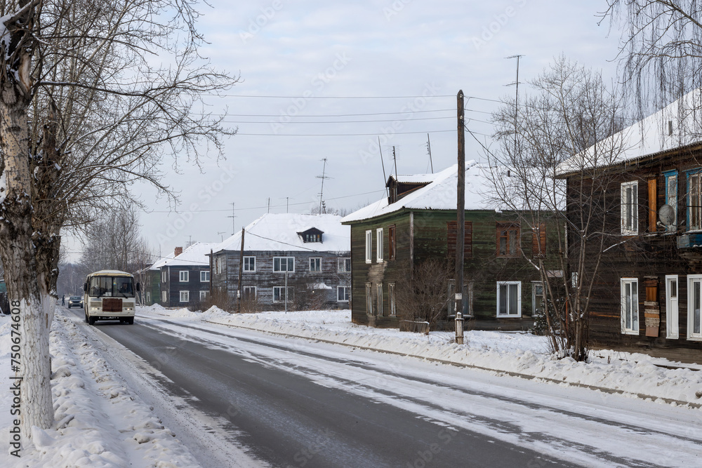 Street in a Siberian city. View of multi-apartment wooden buildings. A bus is driving along the roadway. Everyday life in Siberia. Bratsk, Irkutsk region, Russia. Eastern Siberia. Cold winter weather.