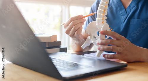 close up physical therapist chiropractor hand pointing on human skeleton at lower back to advise and consult to patient to treatment at office for telemedicine healthcare concept