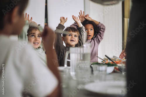 Happy children with arms raised during lunch time at kindergarten photo