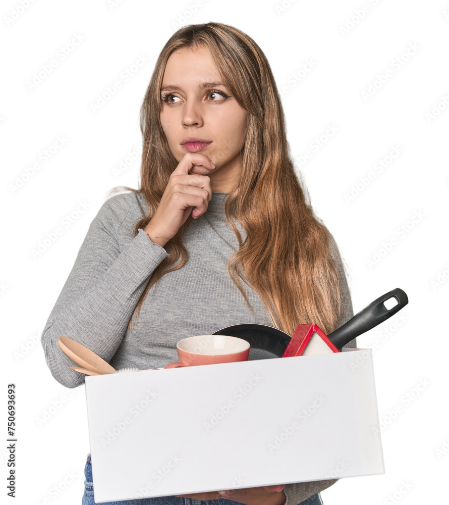 Blonde Caucasian woman moving with a box on studio backdrop looking sideways with doubtful and skeptical expression. - obrazy, fototapety, plakaty 