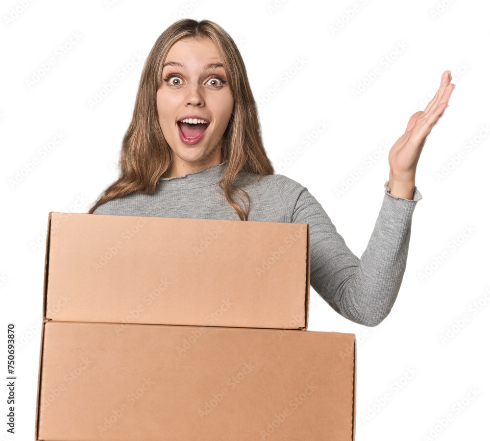 Blonde woman with cardboard boxes moving on studio backdrop receiving a pleasant surprise, excited and raising hands. Blonde woman with cardboard boxes moving on studio backdrop receiving a pleasant surprise, excited and raising hands.