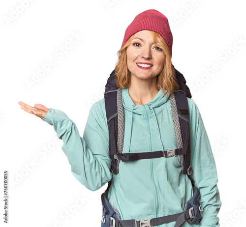 Middle-aged Caucasian woman with hiking gear showing a copy space on a palm and holding another hand on waist.