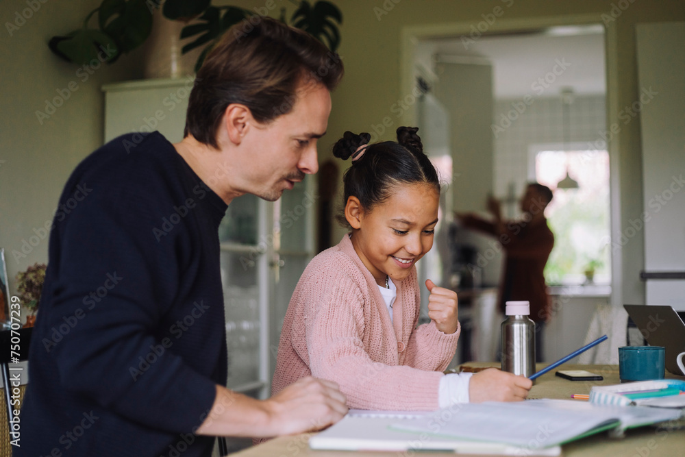 Father sitting next to excited daughter doing homework at home Father sitting next to excited daughter doing homework at home