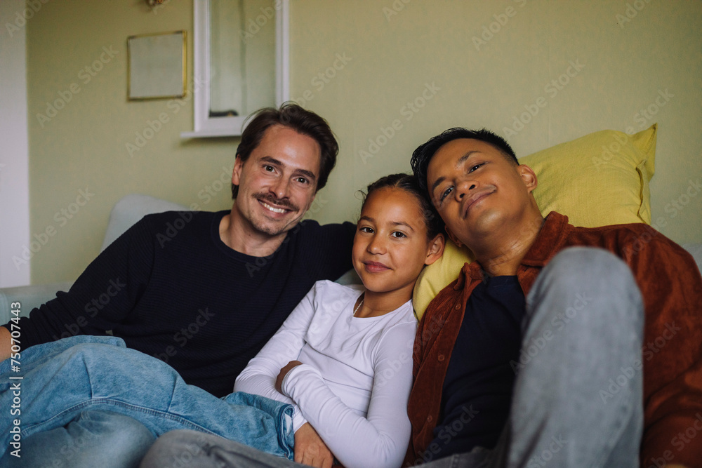 Portrait of smiling gay couple sitting with daughter on sofa at home Portrait of smiling gay couple sitting with daughter on sofa at home