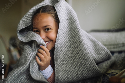 Portrait of playful girl hiding under blanket at home photo