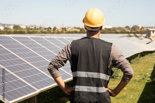Rear view of male engineer with arms akimbo looking at solar panels in field photo