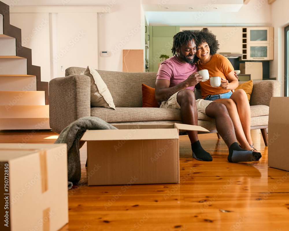 Couple Taking A Break From Unpacking Boxes Sitting On Sofa With Hot Drink In New Home On Moving Day Couple Taking A Break From Unpacking Boxes Sitting On Sofa With Hot Drink In New Home On Moving Day