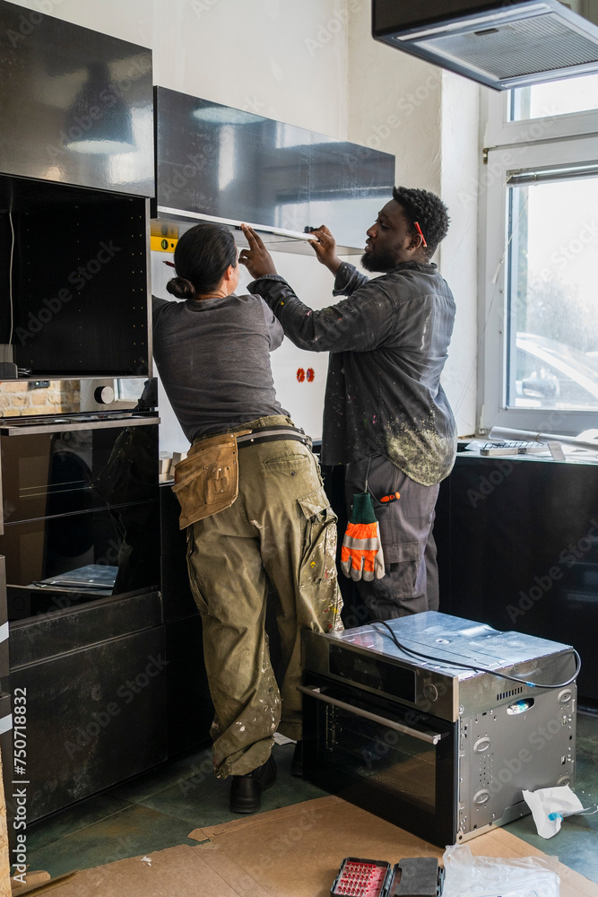 Multiracial male and female carpenters measuring cabinet in kitchen at home Multiracial male and female carpenters measuring cabinet in kitchen at home