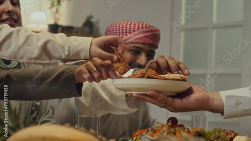 Side footage of unrecognizable hospitable host offering pastry or biscuits to male and female muslim family members during festive dinner on Eid al-Fitr