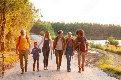 Принти на полотні A heartwarming scene of multigenerational camaraderie is depicted in this image, where a group of friends enjoy a leisurely walk along a country path by the lake as the sun sets
