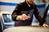 Focus on the mechanic man's hand, repairing the car, using a machine.