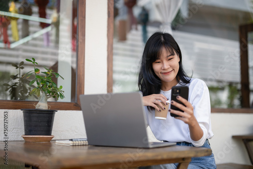 Young Asian woman using smartphone and laptop in outdoor cafe, self-employed