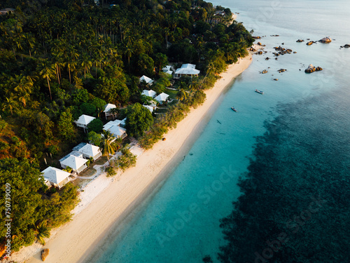 This bird's-eye view reveals a beautiful tropical island. Surrounded by clear turquoise water like glass. The pristine white beaches contrast with the lush greenery of the island's greenery. In the ce